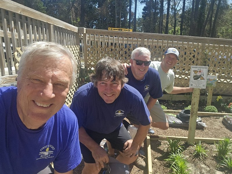 Four First Flight Rotary members smiling in the new garden beds they built at the Children and Youth Partnership Outdoor Learning Environment in Manteo
